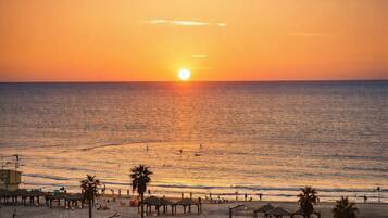 A beach with a sunset, palm trees, and beach umbrellas.
