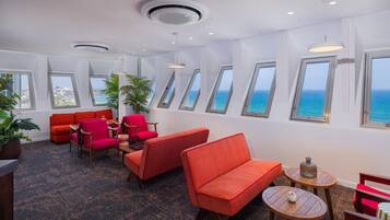 Eine moderne Lounge mit roten Sofas, einem Holztisch und Meerblick durch Dachfenster.