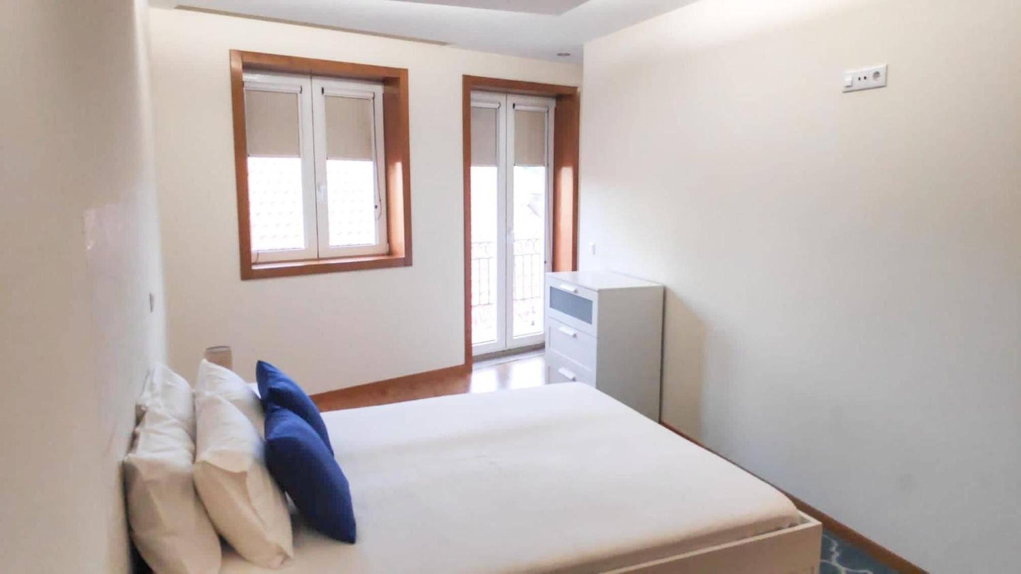 A bedroom with a bed, two windows, a dresser, and a door.