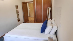 A bedroom with a bed, a wooden wardrobe, and a door.