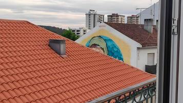 Un balcón con tejado de tejas rojas, barandilla de metal y vista a un edificio con un mural.