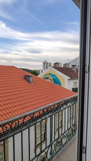 A balcony with a red-tiled roof, a metal railing, and a view of a building with a mural.
