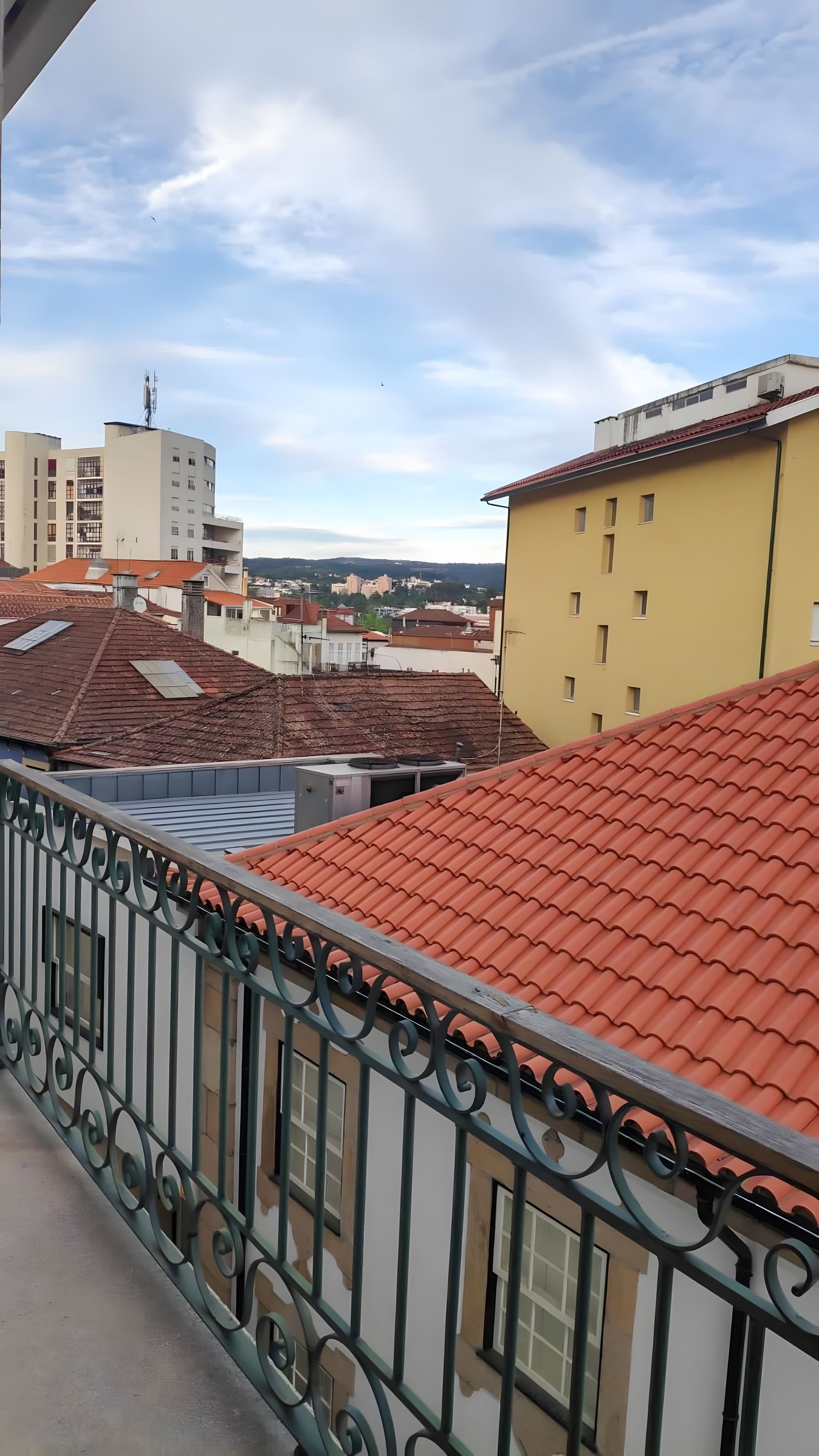 Un balcón con techo de tejas rojas, baranda de metal y vistas de edificios circundantes.