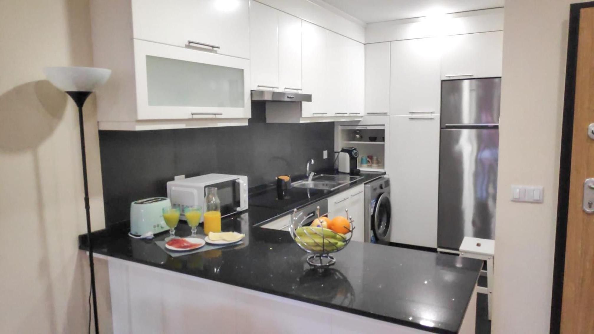 A compact kitchen with a refrigerator, microwave, toaster, sink, and a fruit bowl on the counter.