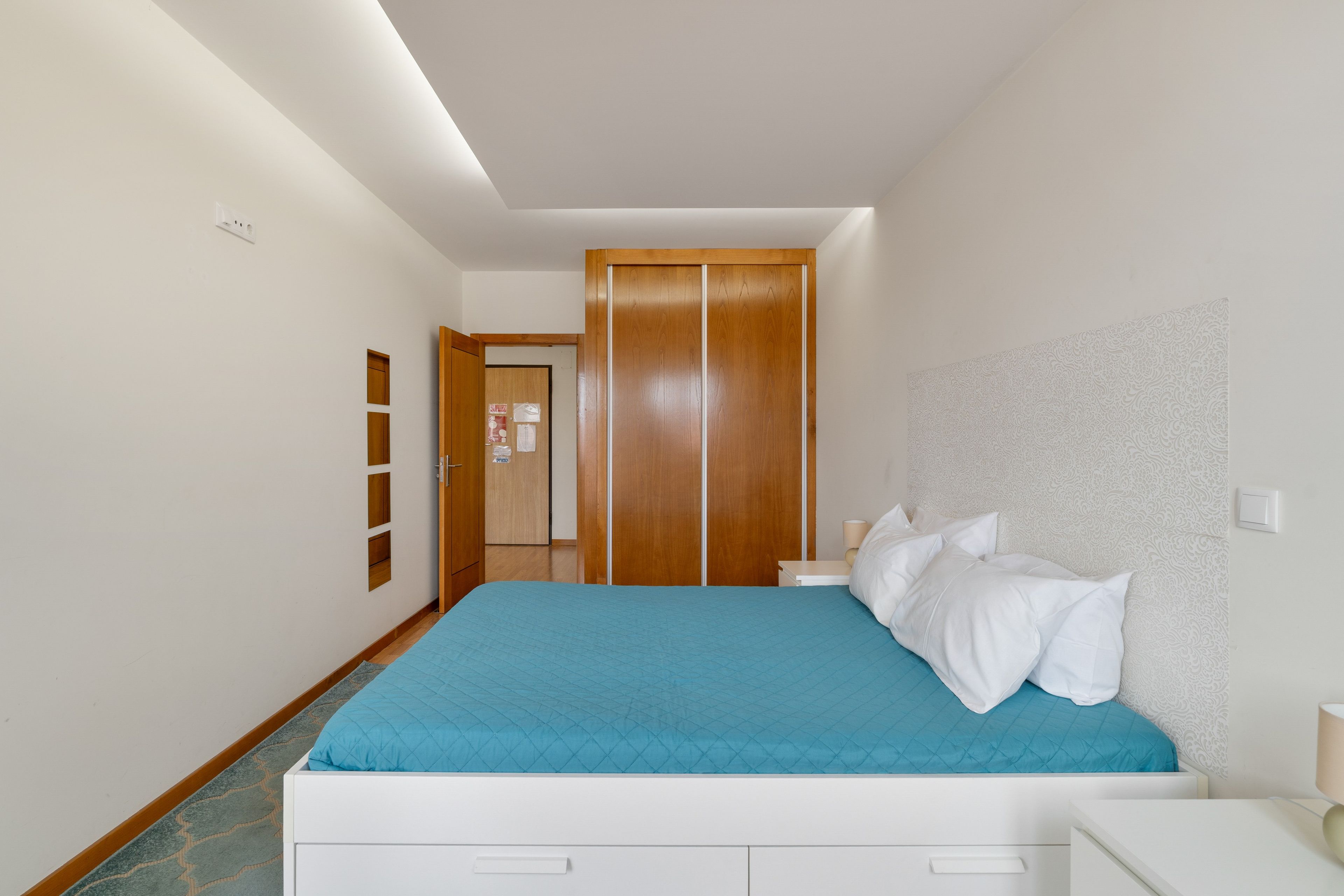 Una habitación de hotel con una cama, mesitas de noche, un armario y un papel tapiz estampado.
