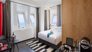 A hotel room with a bed, a small table with a tray of breakfast items, a chair, and a view of the sea through large windows.