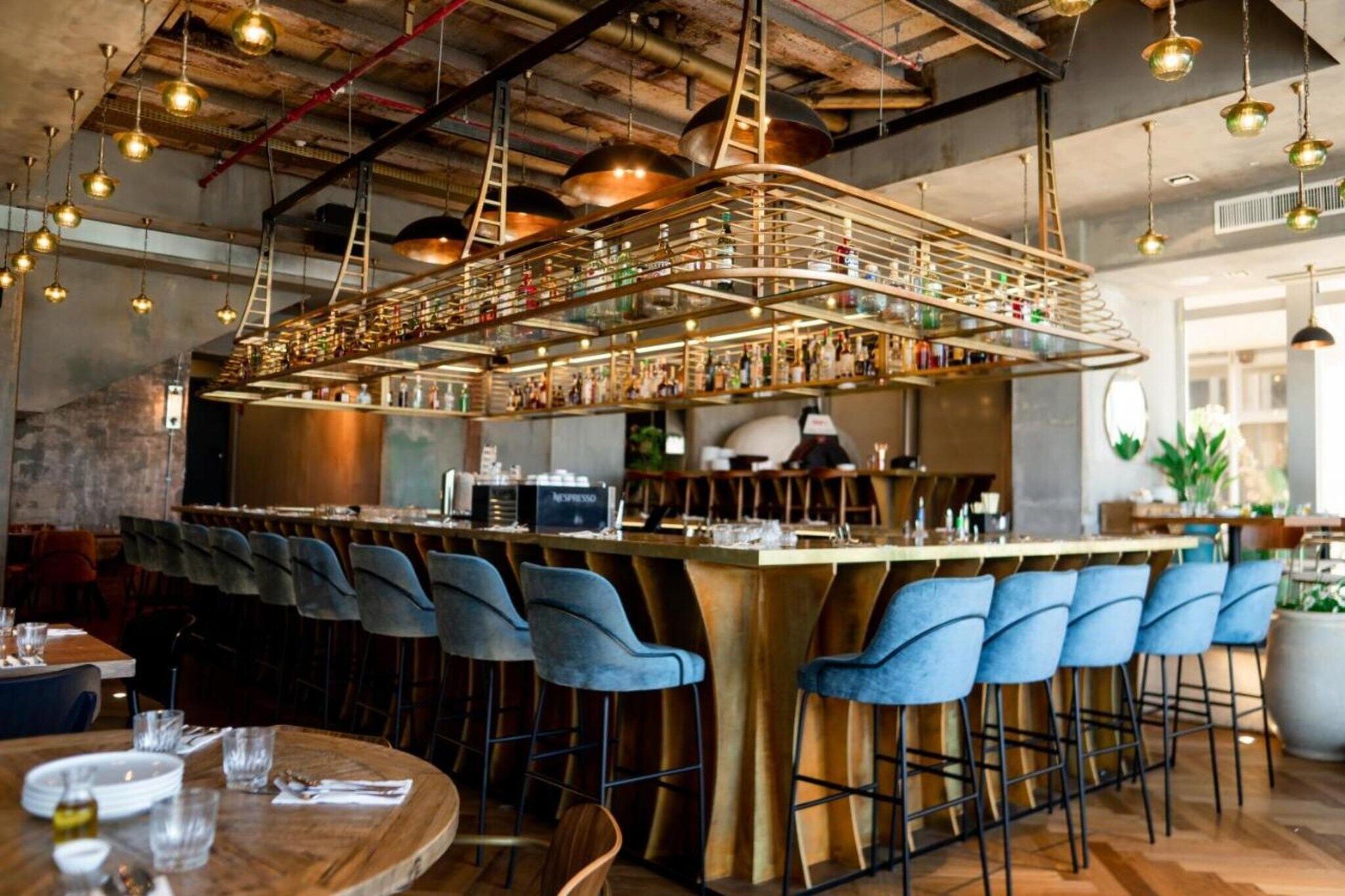 Un espace bar doté d’un long comptoir, de tabourets de bar bleus et de luminaires suspendus.
