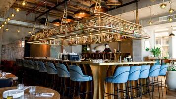 A bar area with a long counter, blue bar stools, and hanging pendant lights.