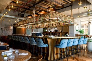 A bar area with a long counter, blue bar stools, and hanging pendant lights. - Dancenter Brut Seafront Hotel Tel Aviv- Executive Double room with Sea view (Tel Aviv)