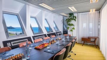 Sala de conferências com uma mesa comprida, cadeiras e vista para o mar através de claraboias.