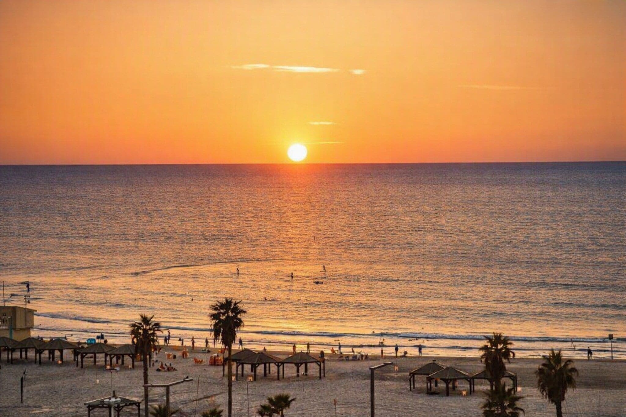 Une plage au coucher du soleil, avec des palmiers et des parasols de plage.