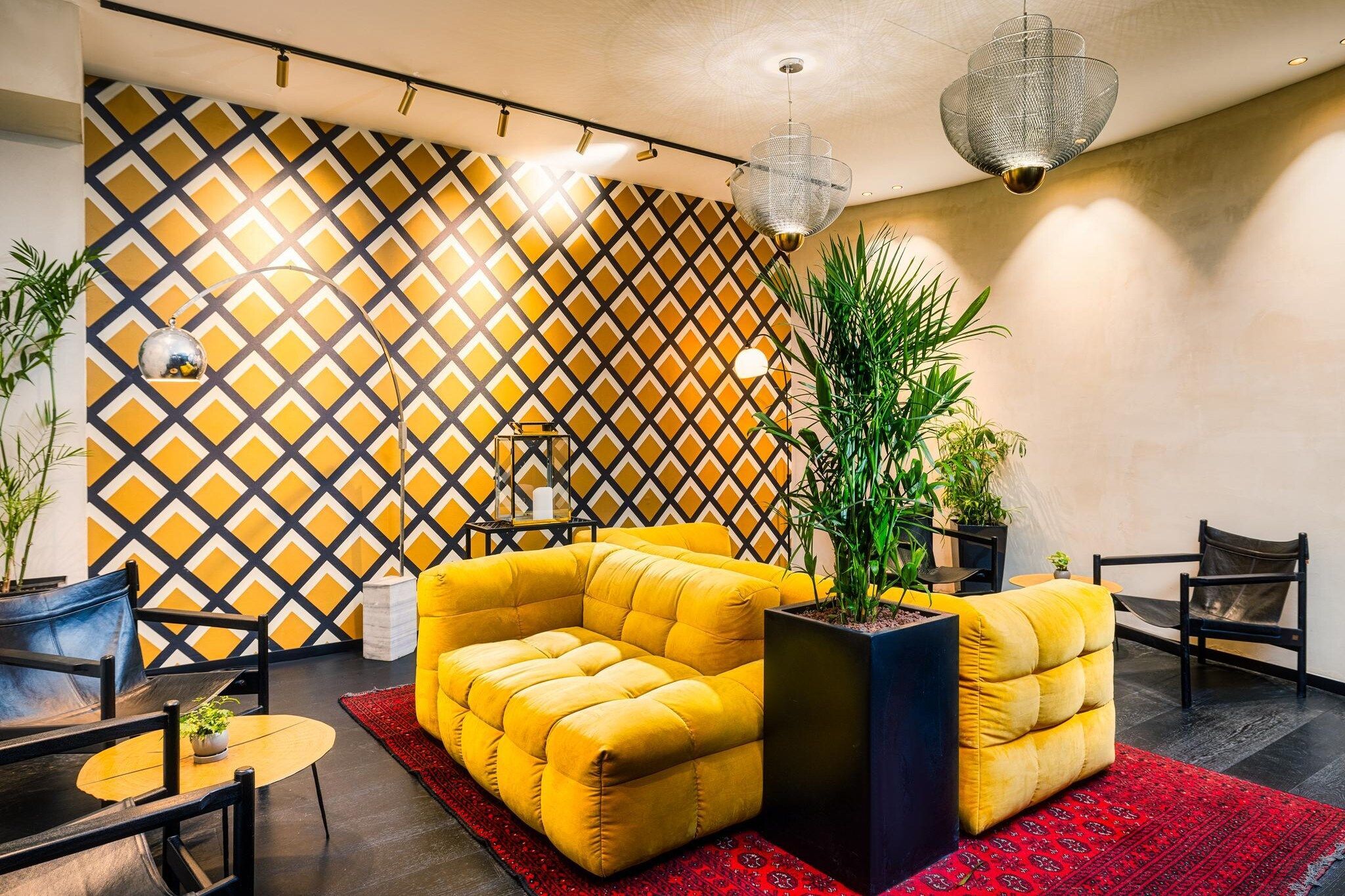 A modern interior with a yellow sofa set, black chairs, a red rug, and a geometric patterned wall.