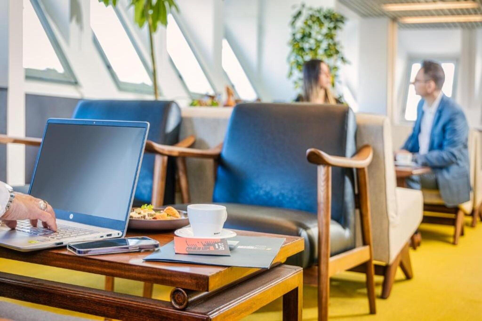 Un hall d’hôtel moderne avec des coins salon, un ordinateur portable posé sur une table et une personne qui travaille.
