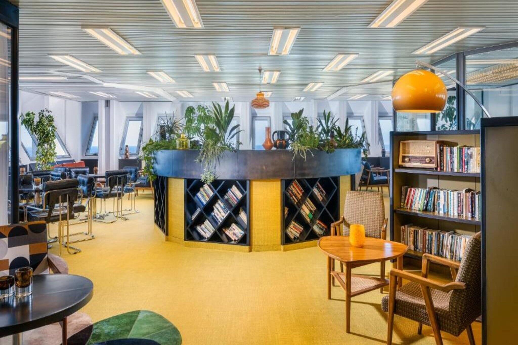 A modern library with a central island, bookshelves, seating areas, and large windows.