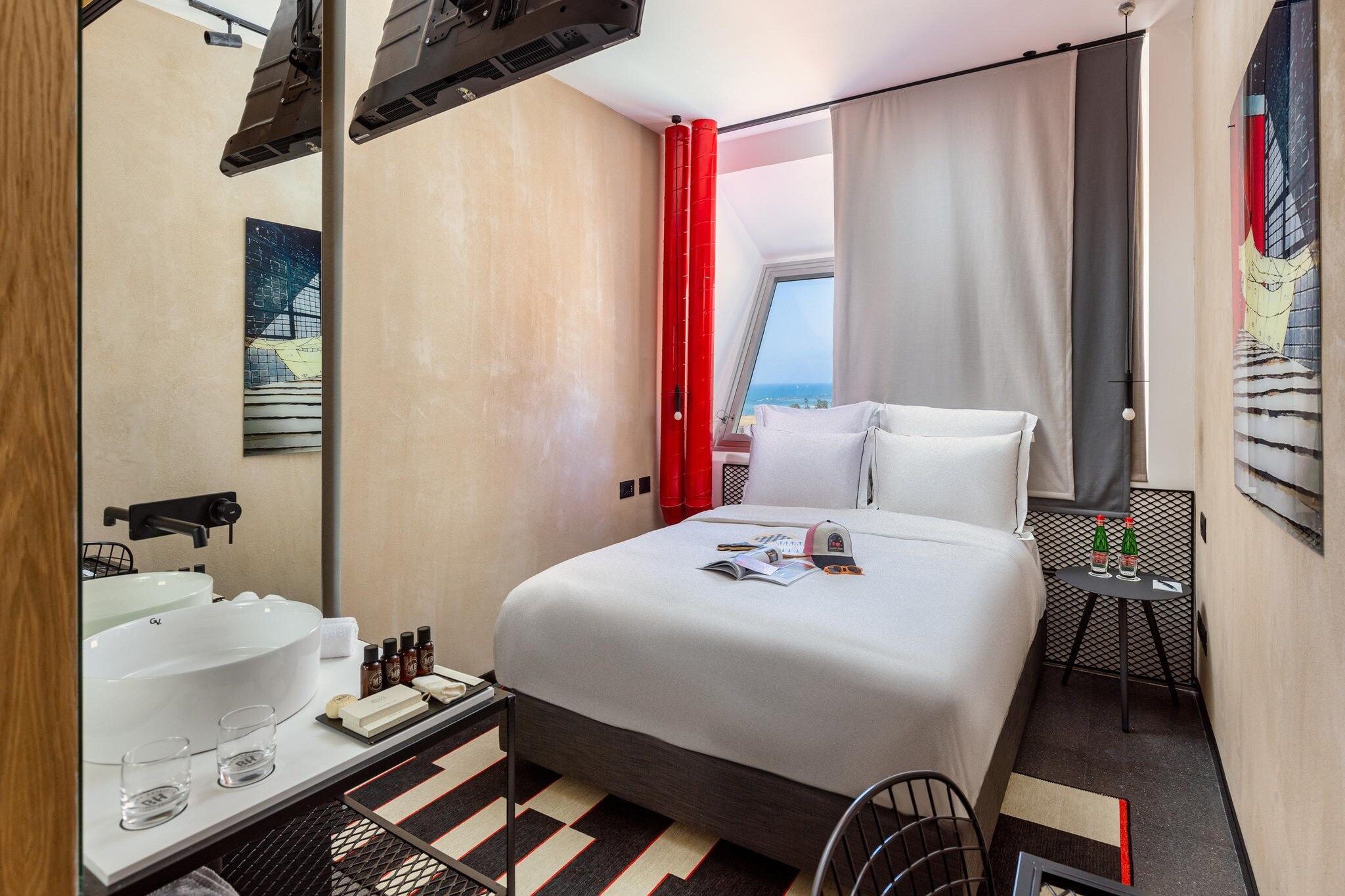 A hotel room with a bed, a bathroom with a sink and mirror, a small table with bottles, and a chair.