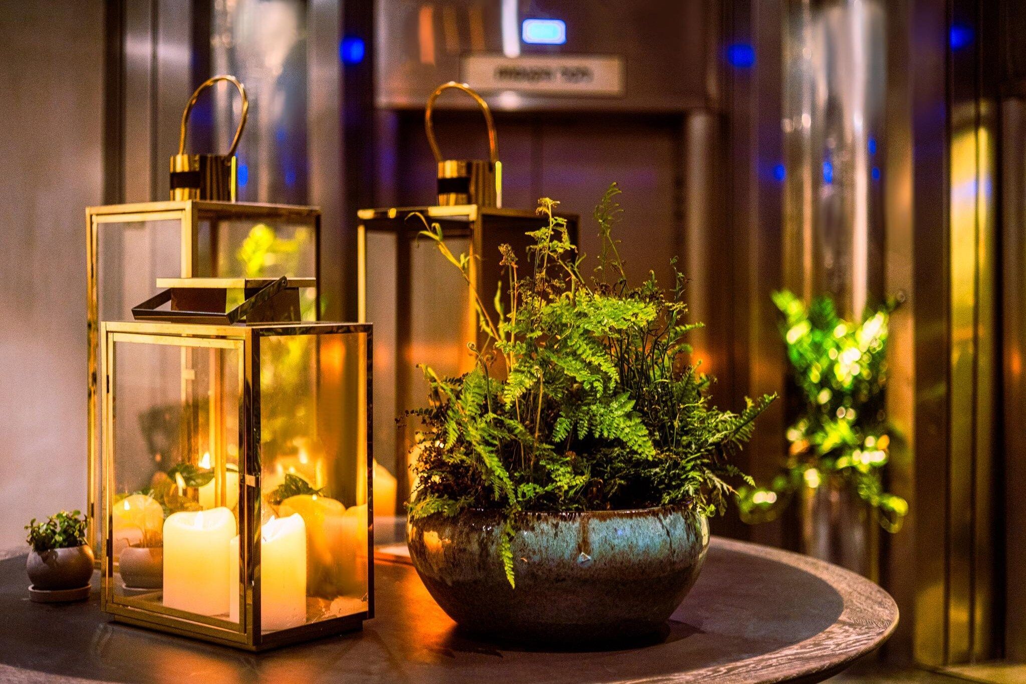 A room with a round table, two lanterns, a potted fern, and candles.