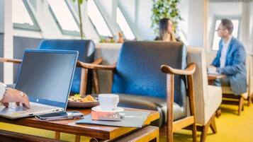 A modern hotel lobby with seating areas, a laptop on a table, and a person working.