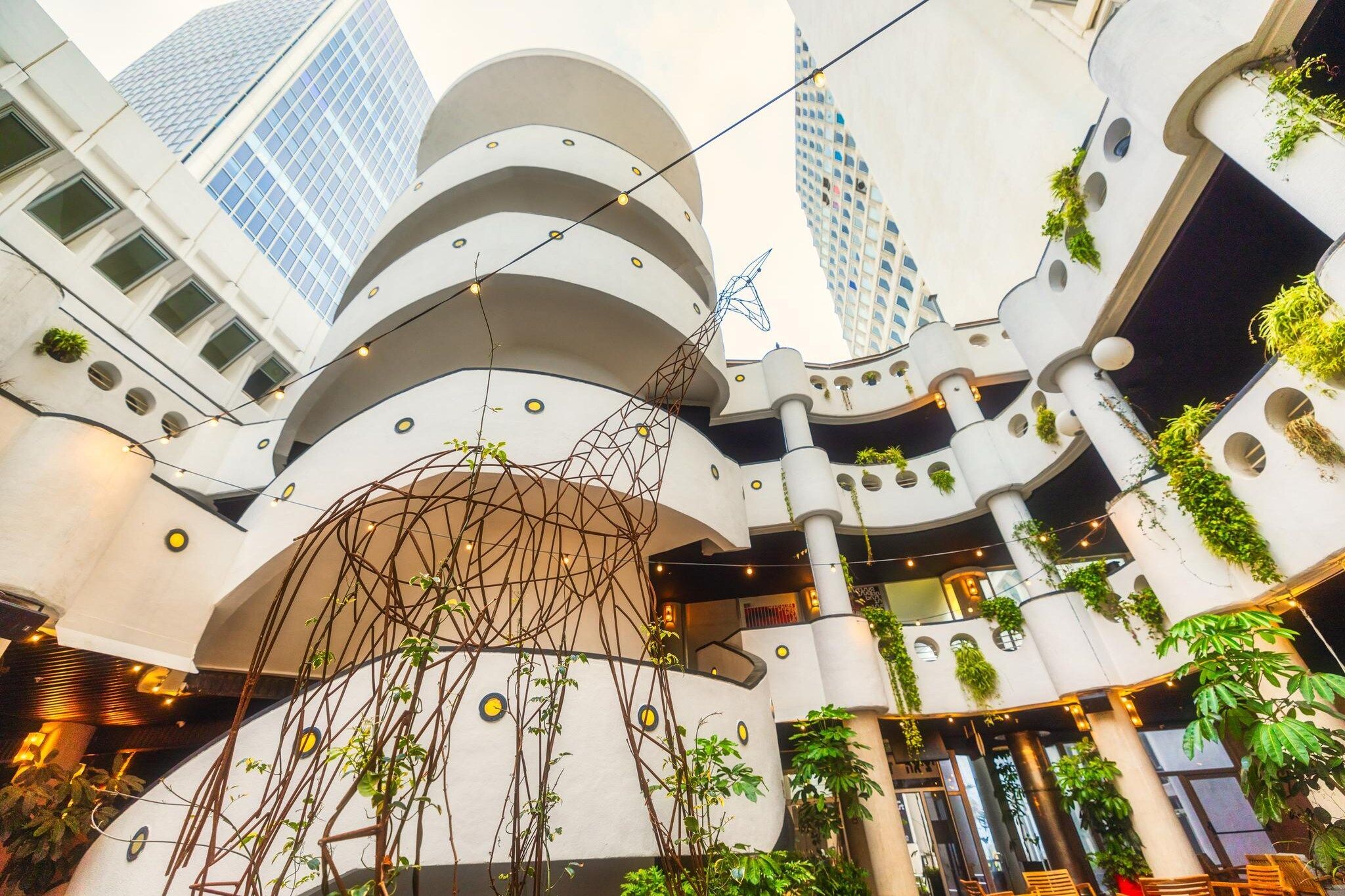 Un atrium à plusieurs niveaux, doté d’une architecture moderne, avec des balcons ornés de plantes et illuminés de guirlandes lumineuses.