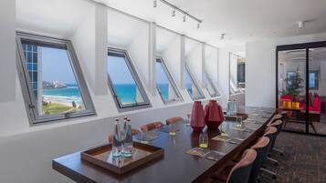 Ein Konferenzraum mit einem langen Tisch, mehreren Stühlen und Meerblick durch Dachfenster.