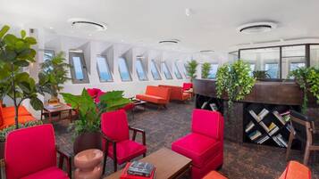 A modern lounge area with red seating, a coffee table, and potted plants.