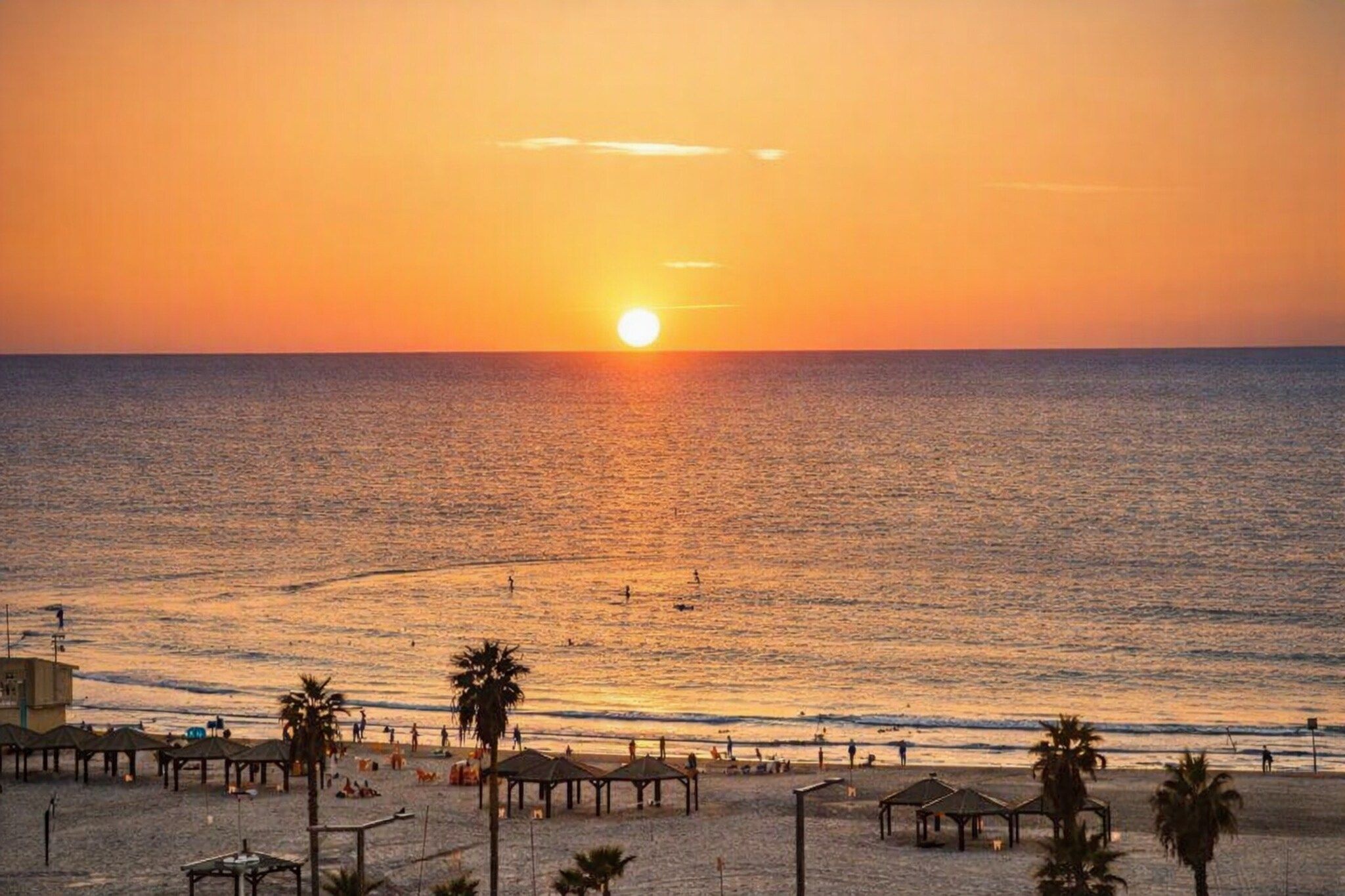 Une plage au coucher du soleil, avec des palmiers et des parasols de plage.