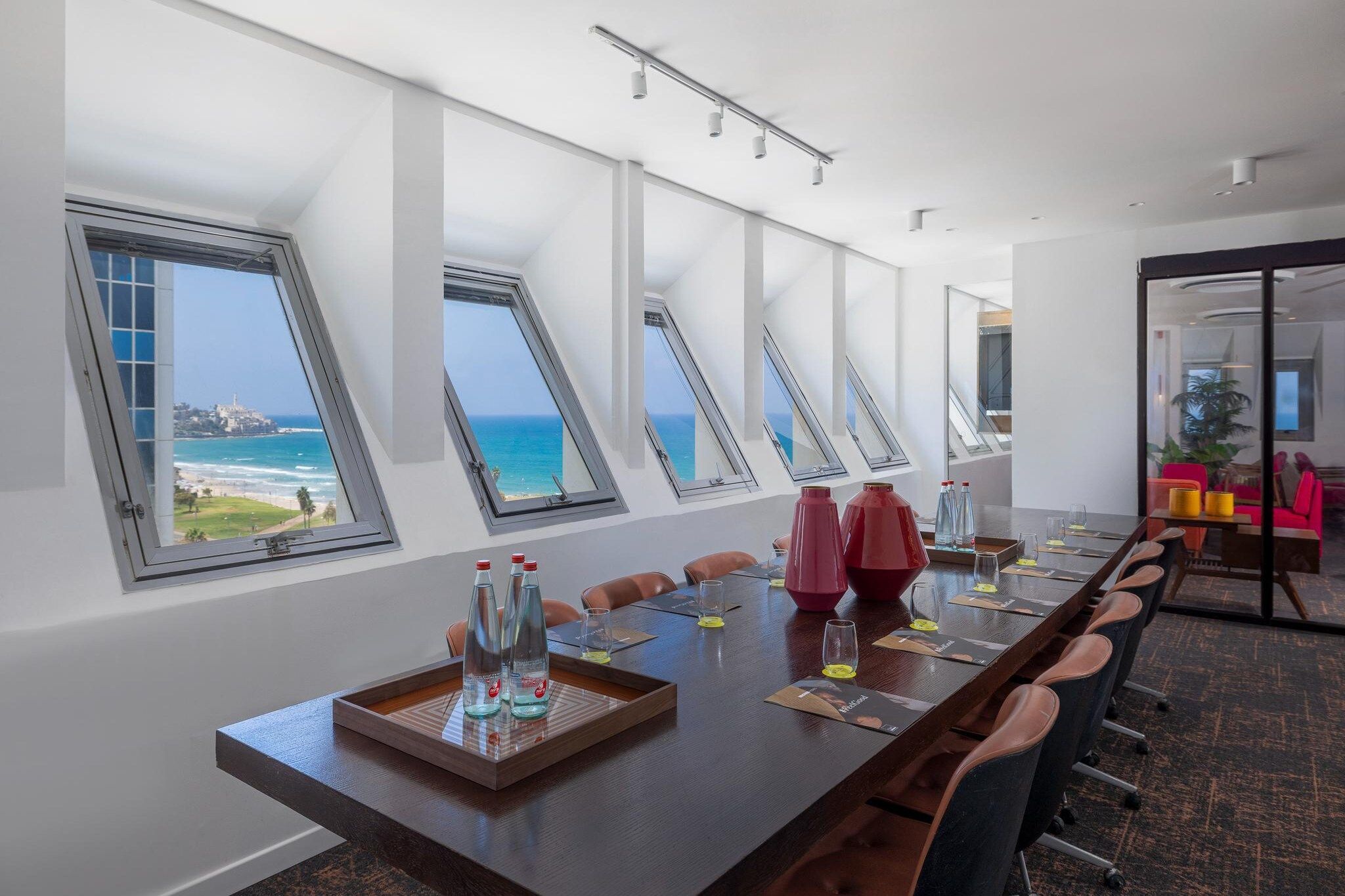 A conference room with a long table, multiple chairs, and a view of the ocean through skylights.
