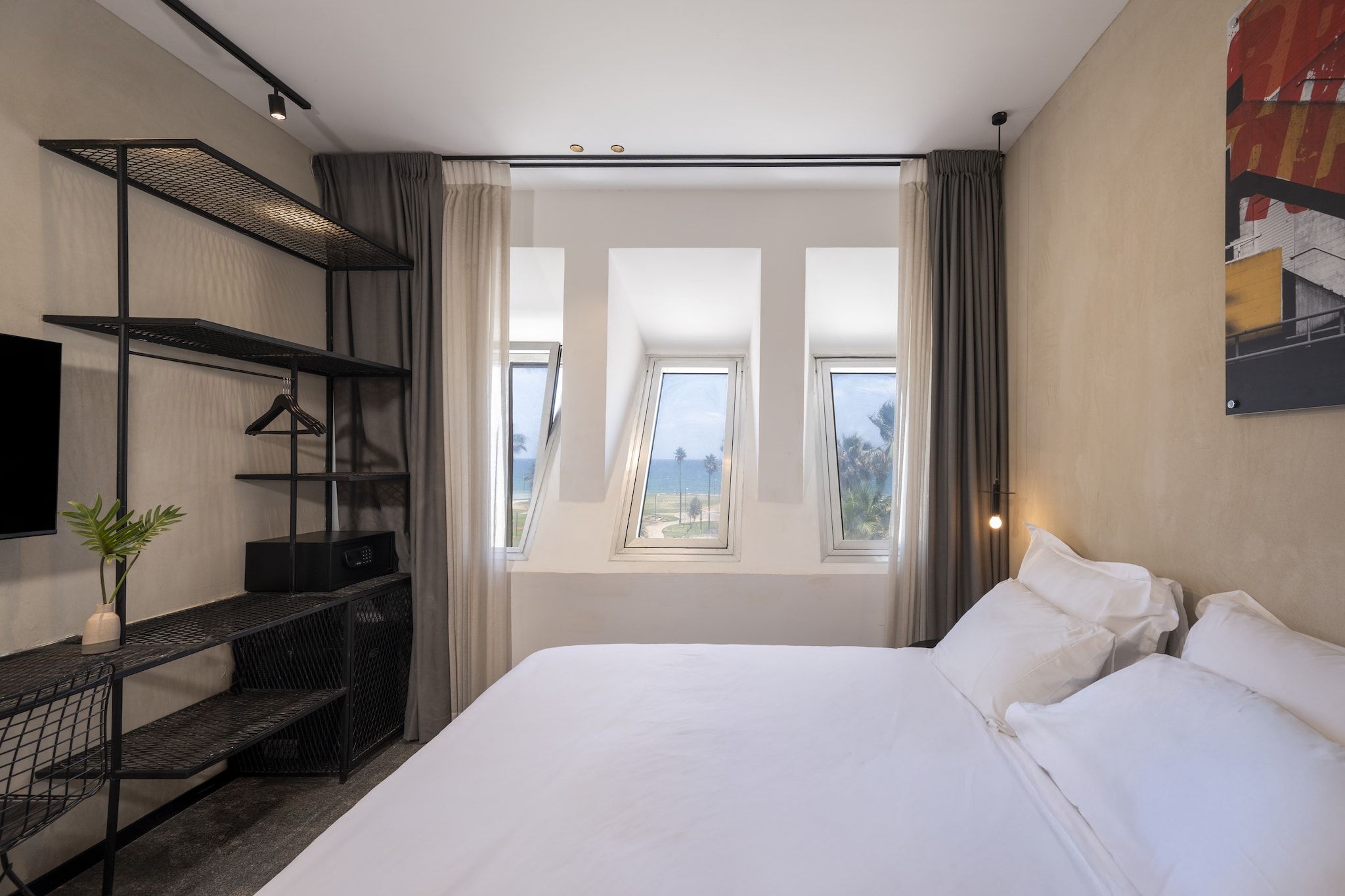 Habitación de hotel con una cama grande, televisión, escritorio con planta y vistas al mar a través de ventanas.