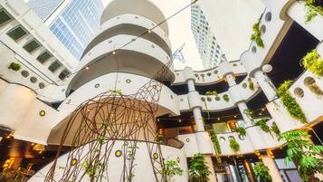 A multi-level atrium with modern architecture, featuring balconies with greenery and string lights.