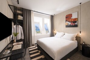 Une chambre d’hôtel avec un lit, un bureau avec un ordinateur portable, une chaise, une plante et une fenêtre donnant sur un paysage.