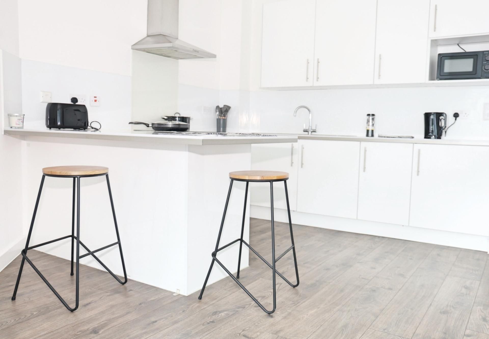 Een moderne keuken met witte kastjes, een magnetron, een fornuis en twee krukken.