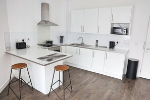A modern kitchen with white cabinetry, a central island, two bar stools, and a microwave on the countertop. - Cozy Croydon Apartment Retreat (Croydon)