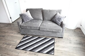 A grey sofa with two patterned cushions in a room with wooden flooring. - Cozy Croydon Apartment Retreat (Croydon)