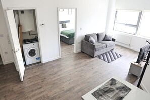 Un apartamento moderno con sofá gris, televisor de pantalla plana y lavadora en un rincón.
