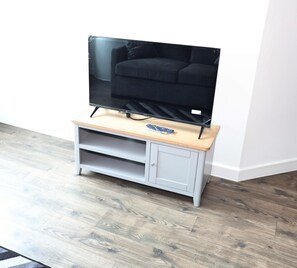 Un televisor de pantalla plana sobre un mueble de madera con un control remoto, un armario gris y un piso de madera.