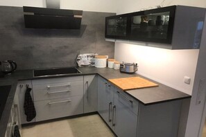 Eine moderne Küche mit grauen Schränken, einer schwarzen Dunstabzugshaube, einer eingebauten Mikrowelle und einem Holzerntisch.