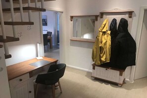 Ein Zimmer mit Schreibtisch, Stuhl und Kleiderhaken mit Jacken.