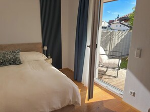 A bedroom with a bed, a nightstand, a lamp, and a view of the outside.