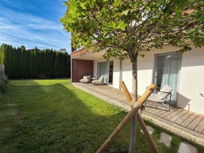 Ett modernt hus med en träaltan, utomhusmöbler och ett träd.