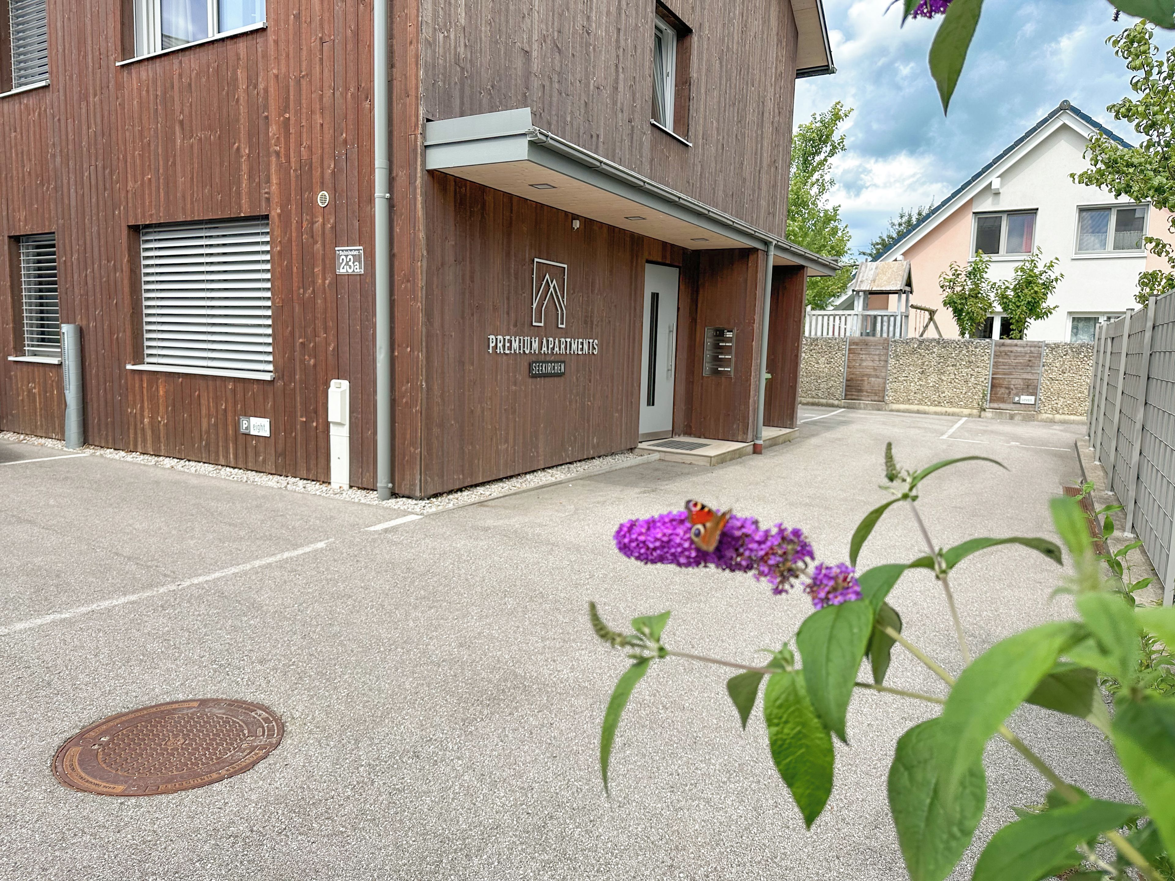 A modern building with a wooden facade, a visible entrance, and a manhole cover on the ground.