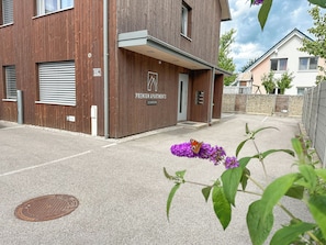 A modern building with a wooden facade, a visible entrance, and a manhole cover on the ground.