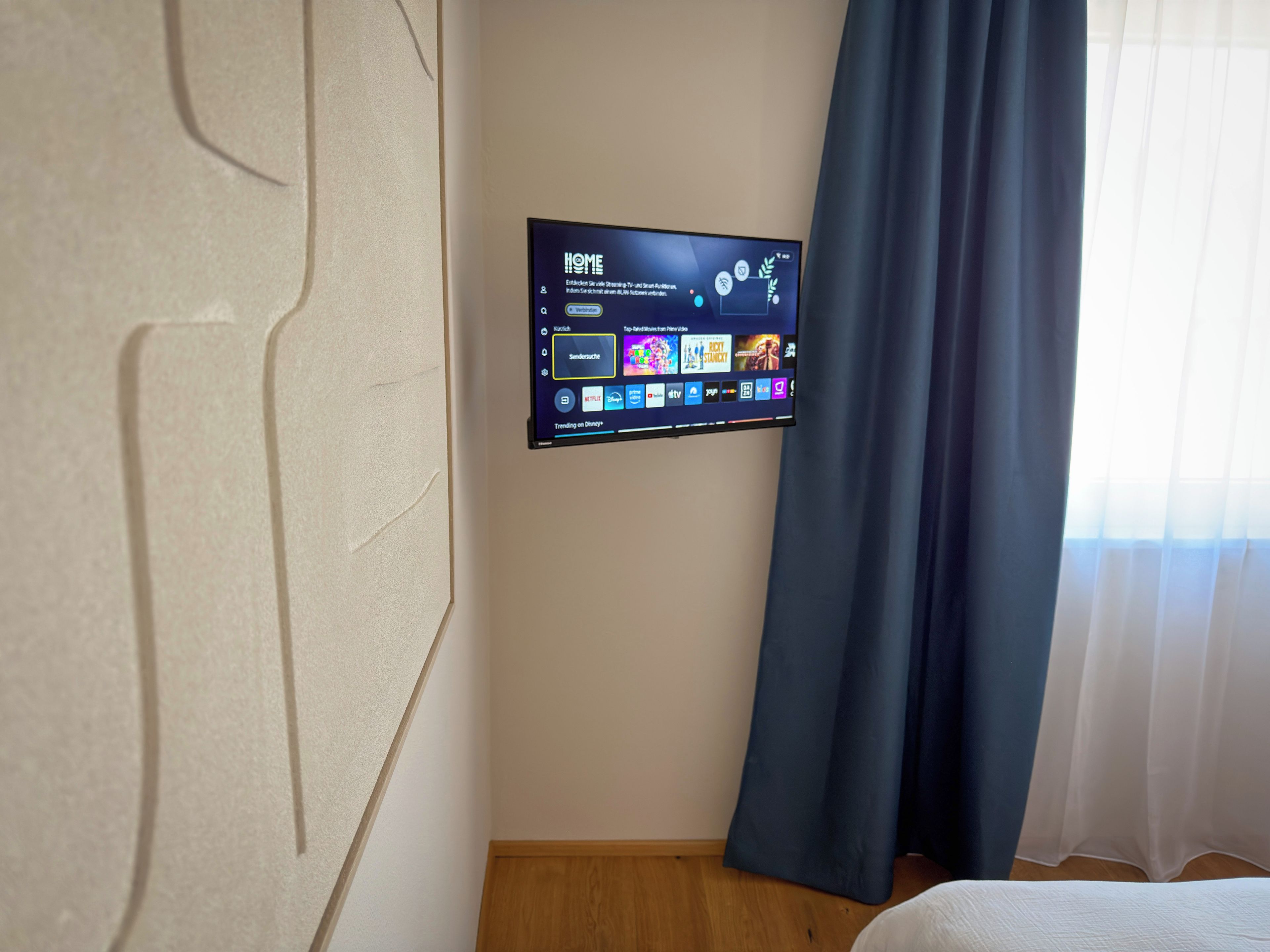 A flat-screen TV mounted on a wall displaying a home screen with various streaming options.