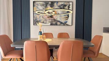 A dining area with a round table, six chairs, a painting on the wall, and a decorative vase with candles.