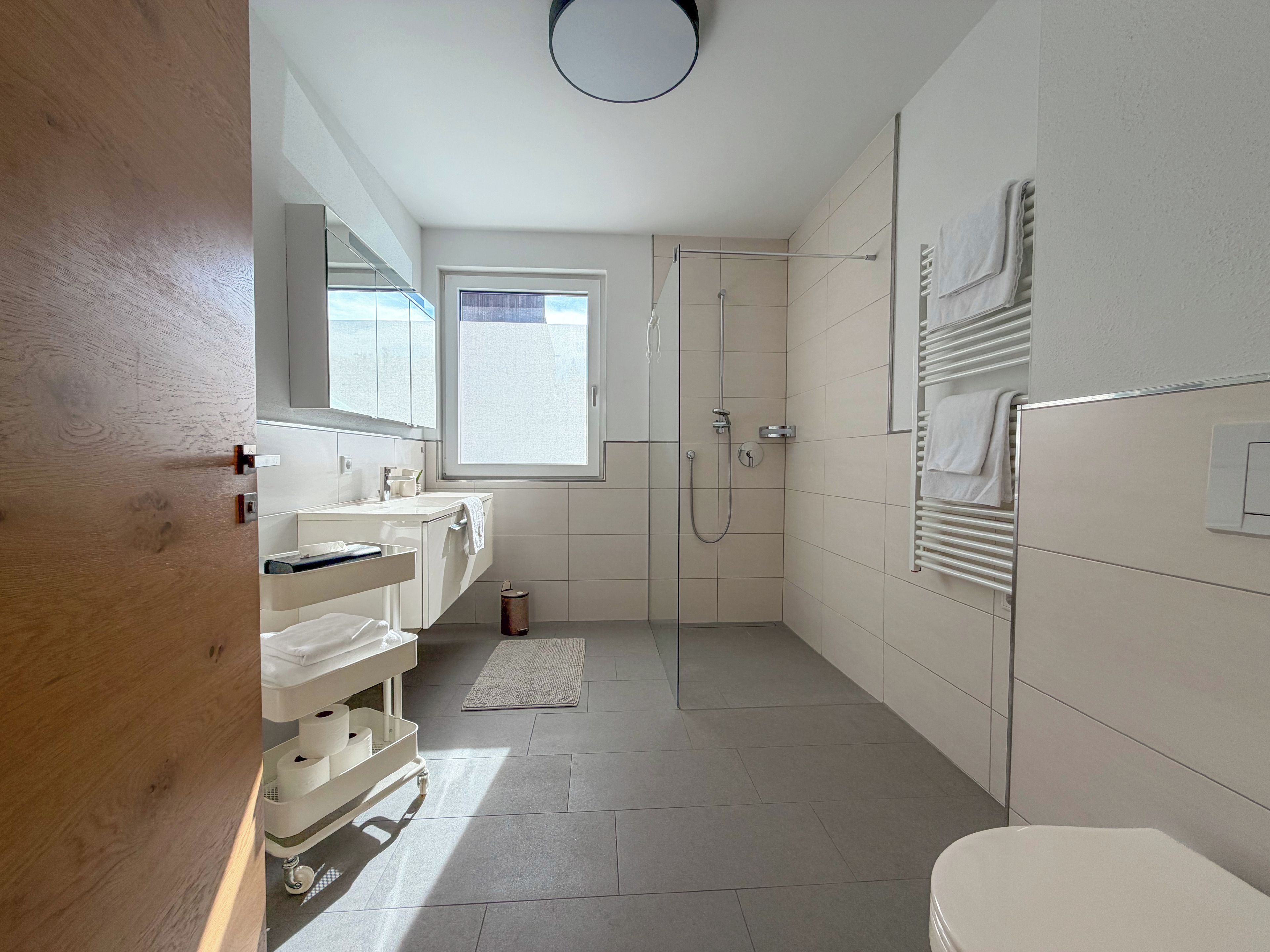 Ein modernes Badezimmer mit Dusche, zwei Waschbecken, Toilette und einem Fenster für natürliches Licht.