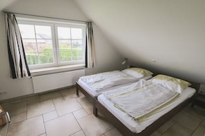 A room with two beds, a window with curtains, a radiator, and a lamp. - The "Heligoland Upper Country" (Wurster Nordseeküste)