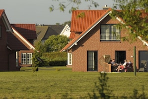 Un quartier résidentiel avec des maisons en briques, une pelouse verdoyante et un groupe de personnes dînant à l’extérieur.