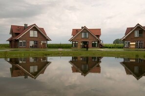 A row of three brick houses with pitched roofs, each with a front door and windows, reflected in a calm water body in front. - The "Heligoland Upper Country" (Wurster Nordseeküste)
