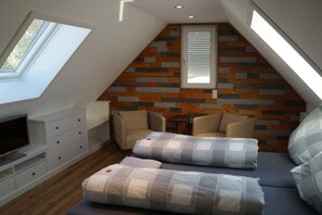 Ein Schlafzimmer im Loft-Stil mit geneigter Decke, integriertem Fernseher, einer Couch und einem gemusterten Kissen.