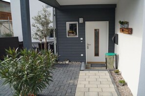 Ein modernes Äußeres mit einer dunkel gefärbten Tür, einem kleinen Fenster mit Pflanze und einem Blumentopf im Vordergrund.