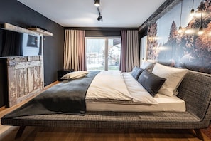 A modern bedroom with a large bed, a mounted television, and a scenic view through the window. - Holiday apartment in Oberstdorf with Wi-Fi (Oberstdorf)