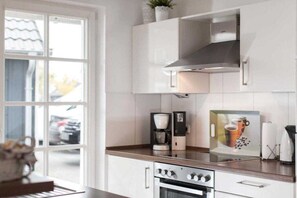 Een moderne keuken met witte kasten, een roestvrijstalen afzuigkap, een koffiezetapparaat en een lijst met een foto op het aanrecht.